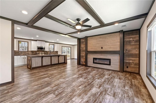 unfurnished living room with visible vents, beam ceiling, a sink, dark wood-style floors, and a fireplace