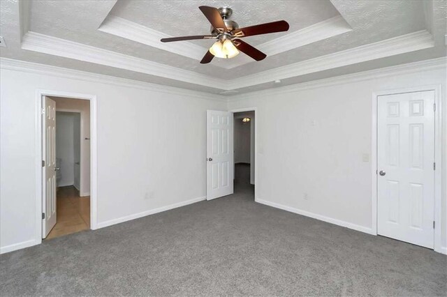 unfurnished bedroom with dark colored carpet, a tray ceiling, ceiling fan, and crown molding