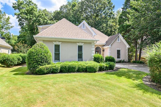 view of front of home with a front lawn, a shingled roof, and stucco siding