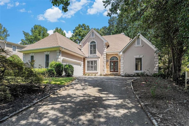 traditional-style house with a garage, a shingled roof, concrete driveway, french doors, and stucco siding