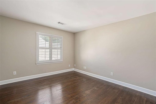 spare room with visible vents, baseboards, and dark wood-type flooring