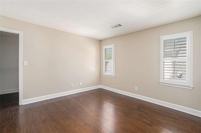 empty room featuring dark wood-style floors, visible vents, and baseboards