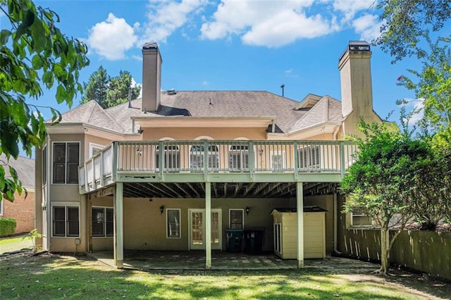 back of property with a lawn, a chimney, a wooden deck, and stucco siding