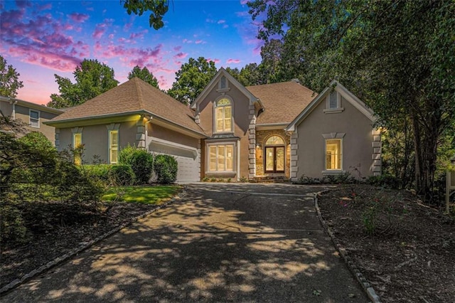 traditional-style home featuring a garage, concrete driveway, a shingled roof, and stucco siding