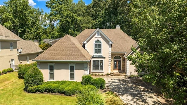 view of front of home featuring driveway, a chimney, roof with shingles, a front yard, and stucco siding