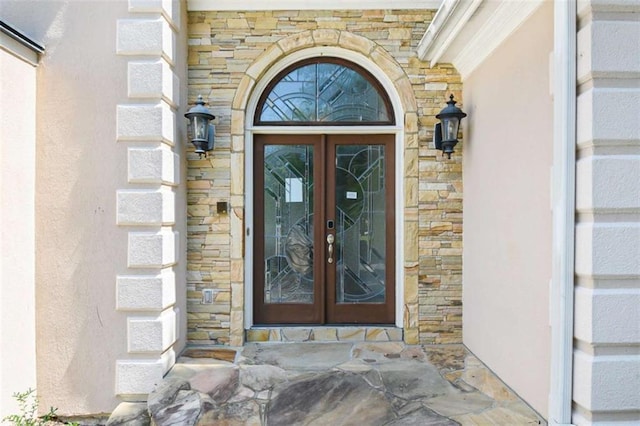 doorway to property featuring stone siding, french doors, and stucco siding