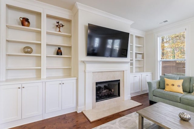 living room featuring built in shelves, a premium fireplace, dark wood-type flooring, and ornamental molding