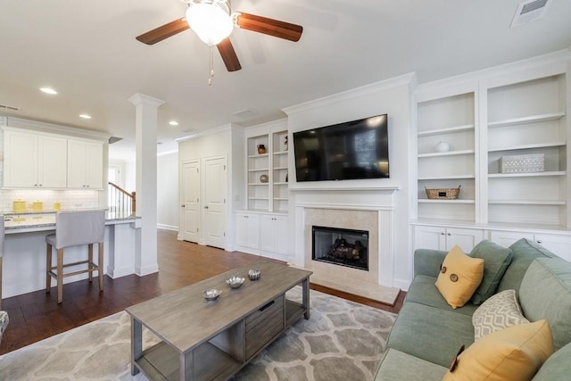 living room with built in shelves, ceiling fan, and dark wood-type flooring