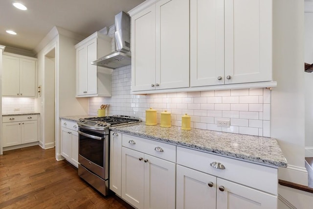 kitchen featuring stainless steel gas stove, wall chimney range hood, dark hardwood / wood-style floors, decorative backsplash, and white cabinets