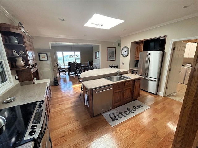 kitchen with sink, washing machine and dryer, appliances with stainless steel finishes, light hardwood / wood-style flooring, and a center island with sink