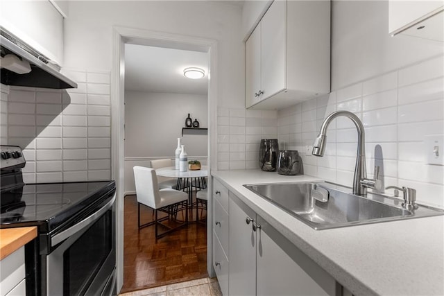 kitchen with parquet floors, electric stove, sink, ventilation hood, and white cabinets