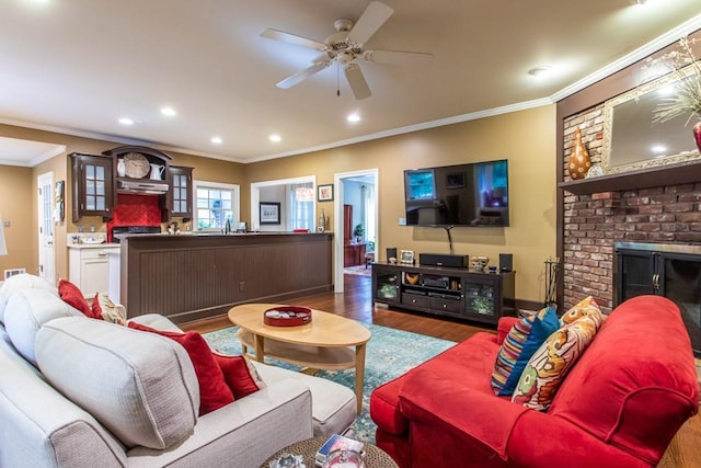 living room featuring ornamental molding, ceiling fan, a brick fireplace, and dark wood-type flooring