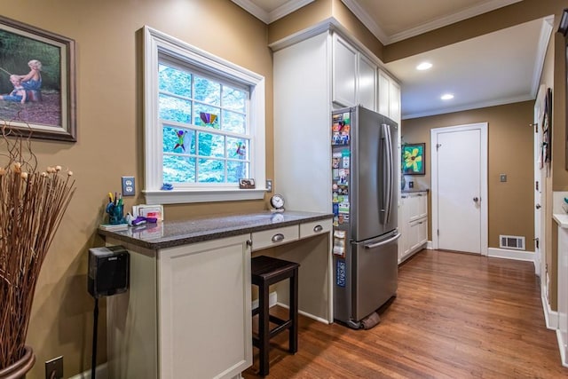 kitchen featuring stainless steel refrigerator, dark wood-type flooring, a breakfast bar, white cabinets, and ornamental molding