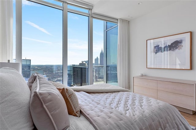 bedroom featuring light wood finished floors, a view of city, and a wall of windows