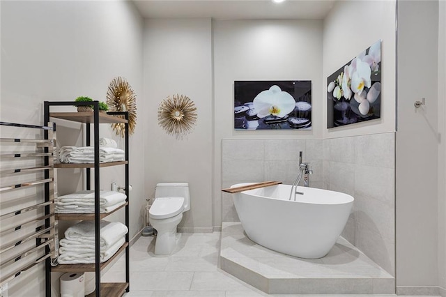 bathroom featuring tile patterned floors, a freestanding tub, toilet, and tile walls