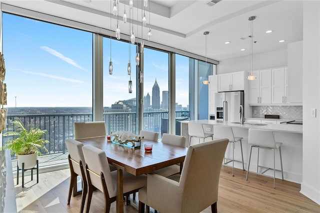 dining area with a wall of windows, a view of city, light wood-style flooring, and a healthy amount of sunlight