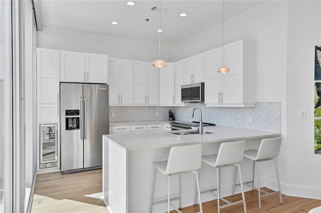 kitchen with backsplash, light wood-style flooring, appliances with stainless steel finishes, a peninsula, and a sink