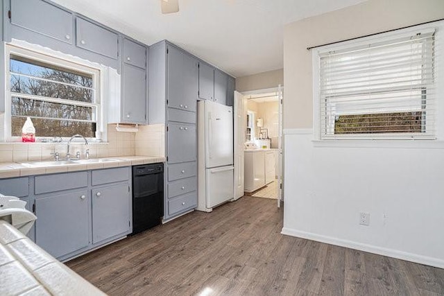 kitchen featuring dishwasher, sink, white refrigerator, tile counters, and washing machine and dryer