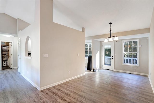 entryway featuring baseboards, vaulted ceiling, wood finished floors, and an inviting chandelier