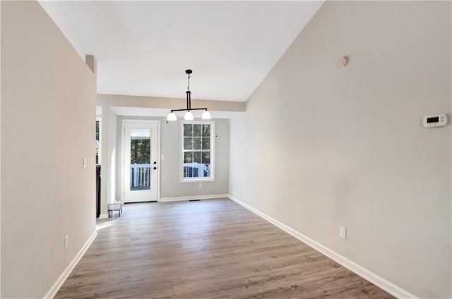 unfurnished dining area featuring baseboards, vaulted ceiling, and wood finished floors