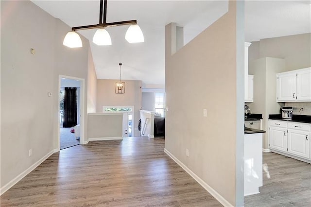 interior space featuring dark countertops, high vaulted ceiling, light wood-type flooring, and white cabinetry