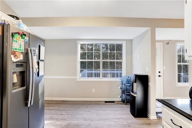kitchen featuring white cabinetry, stainless steel refrigerator with ice dispenser, baseboards, dark countertops, and light wood-style flooring