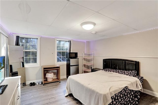 bedroom featuring baseboards, wood finished floors, and freestanding refrigerator