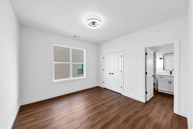 unfurnished bedroom with a closet, ensuite bathroom, and dark wood-type flooring