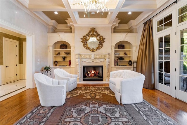 living area featuring built in shelves, wood-type flooring, coffered ceiling, and an inviting chandelier