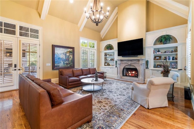 living room with an inviting chandelier, high vaulted ceiling, light wood-type flooring, a high end fireplace, and beam ceiling