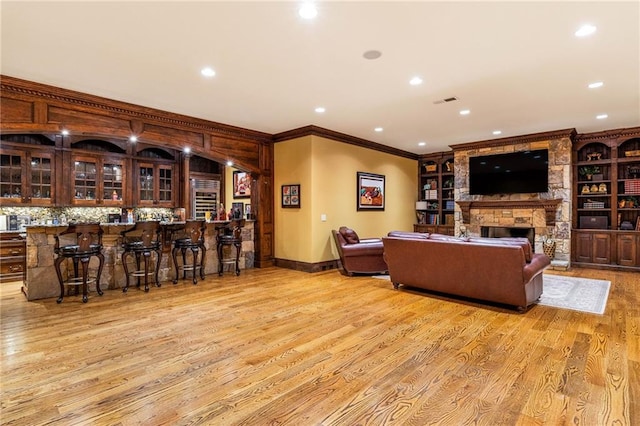 living room with ornamental molding, a stone fireplace, bar area, and light hardwood / wood-style floors