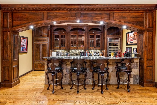 bar featuring lofted ceiling, tasteful backsplash, refrigerator, light hardwood / wood-style flooring, and dark stone counters