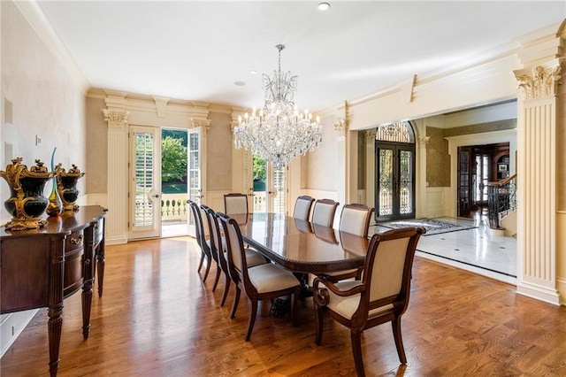 dining area with french doors, crown molding, a chandelier, hardwood / wood-style flooring, and decorative columns