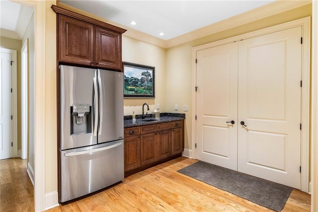 kitchen with sink, dark stone countertops, ornamental molding, stainless steel fridge, and light hardwood / wood-style floors