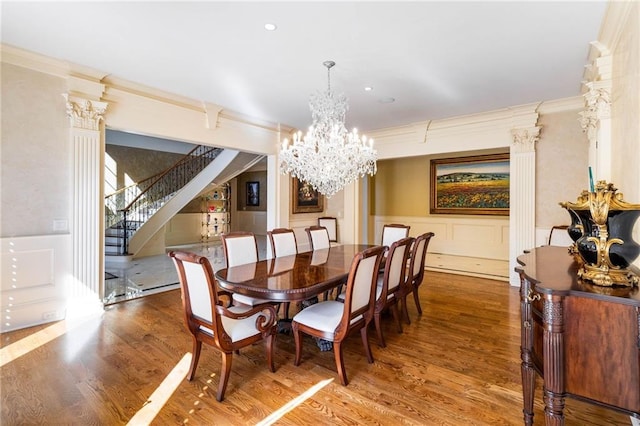 dining space with an inviting chandelier, hardwood / wood-style floors, crown molding, and ornate columns