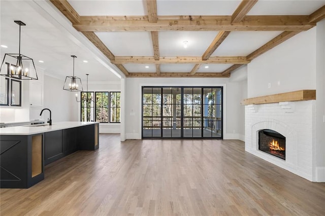 unfurnished living room with light wood-type flooring, a brick fireplace, a sink, and baseboards