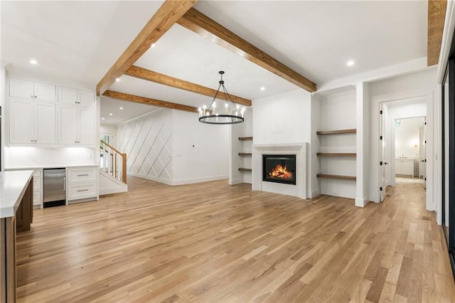 unfurnished living room featuring a glass covered fireplace, stairs, light wood-style floors, beam ceiling, and recessed lighting