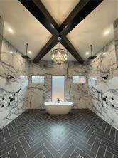 bathroom with brick floor, beamed ceiling, a freestanding bath, and a marble finish shower