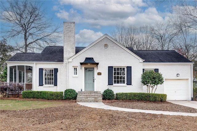 view of front of property featuring brick siding, a sunroom, concrete driveway, roof with shingles, and a chimney