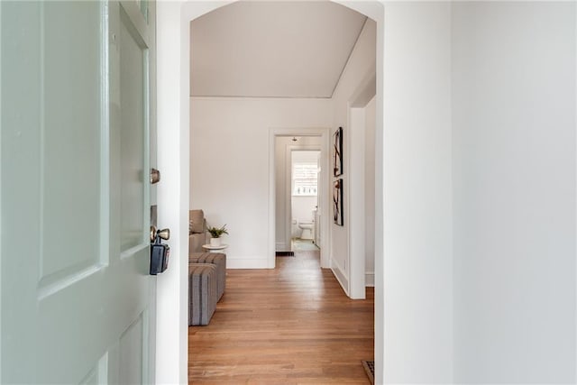 hallway with arched walkways, light wood-style flooring, and baseboards