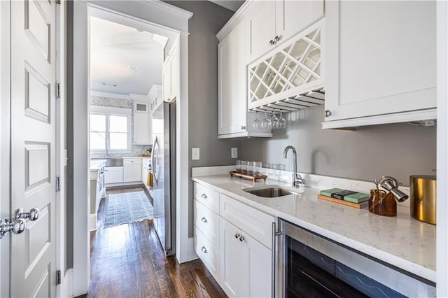 kitchen with wine cooler, white cabinets, freestanding refrigerator, and a sink