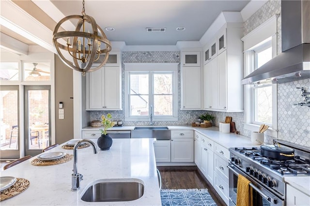 kitchen with visible vents, a sink, high end stainless steel range oven, wall chimney range hood, and glass insert cabinets