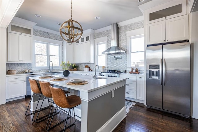 kitchen with appliances with stainless steel finishes, light countertops, wall chimney exhaust hood, and a sink