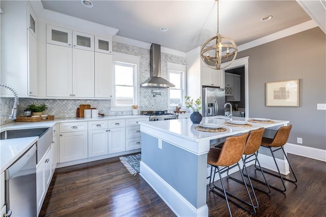 kitchen featuring baseboards, stainless steel appliances, light countertops, glass insert cabinets, and wall chimney range hood