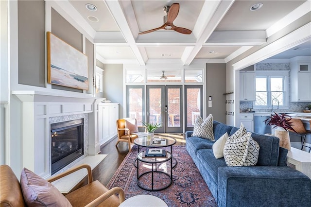 living area with dark wood finished floors, beamed ceiling, french doors, coffered ceiling, and a ceiling fan