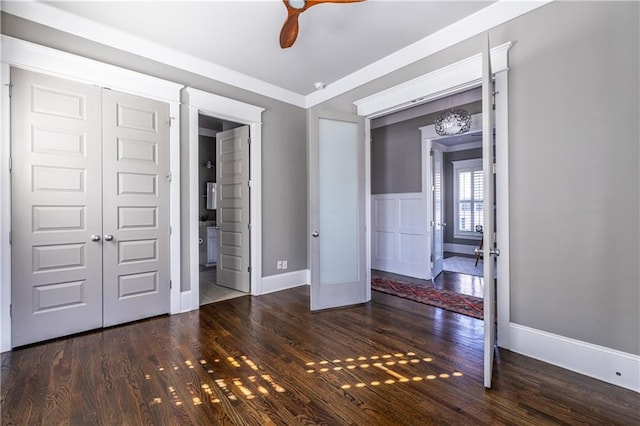 unfurnished bedroom with ensuite bathroom, wood finished floors, a closet, wainscoting, and ceiling fan