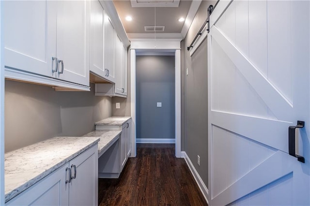 kitchen featuring visible vents, dark wood-type flooring, baseboards, a barn door, and light stone counters