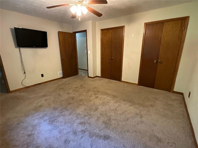 unfurnished bedroom featuring ceiling fan, light colored carpet, and multiple closets