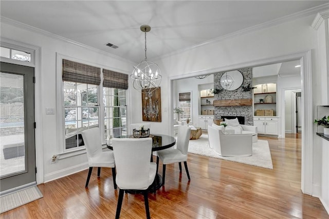 dining room with crown molding, a stone fireplace, light hardwood / wood-style flooring, and built in features