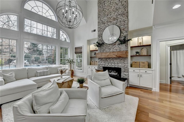 living room featuring built in features, a high ceiling, a fireplace, a chandelier, and light wood-type flooring